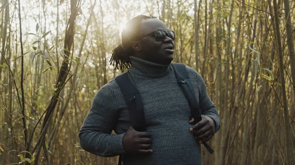 Ung afrikansk amerikansk svart man resenär med ryggsäck går genom skogen — Stockfoto
