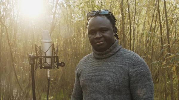 Mladý africký černoch zpívající v mikrofonu v lese. Přírodní světlo — Stock fotografie