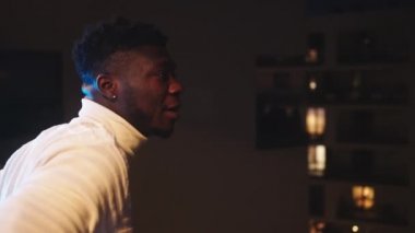 Genç Afrikalı Amerikalı siyahi adam balkonda dikiliyor ve mesafeye bakıyor. Kilitleme sırasında sessiz zaman