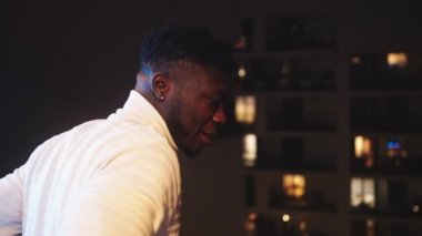 Genç Afrikalı Amerikalı siyahi adam balkonda tek başına dikiliyor ve mesafeye bakıyor. Karantina ve zihinsel sağlık sorunları