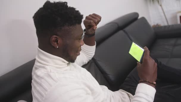 Junger aufgeregter schwarzer Mann schaut Fußballspiel auf dem Smartphone — Stockvideo
