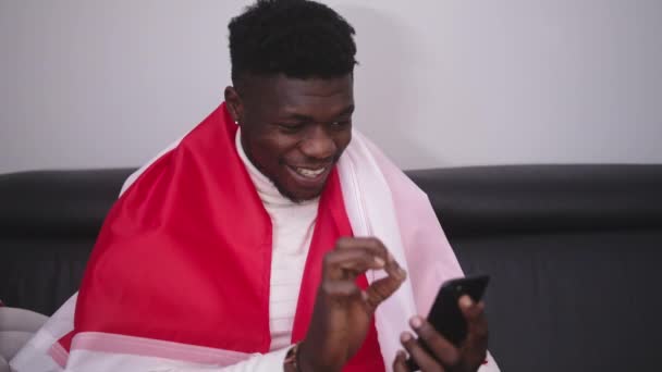 Jovem negro com bandeira polonesa assistindo jogo streaming no smartphone — Vídeo de Stock