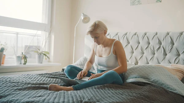 Yatak odasında dizüstü bilgisayar kullanan genç bir kadın. Uzaklık öğrenme kavramı — Stok fotoğraf