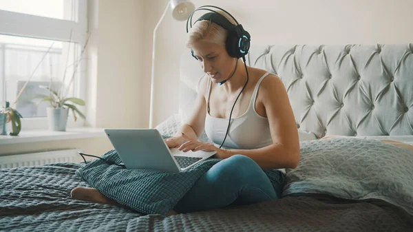Joven mujer rubia caucásica con auriculares juego en el portátil en su dormitorio — Foto de Stock