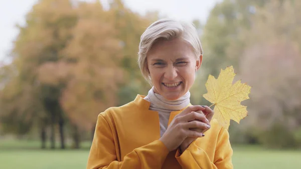 Junge blonde Kaukasierin mit gelbem Herbstblatt im Park — Stockfoto