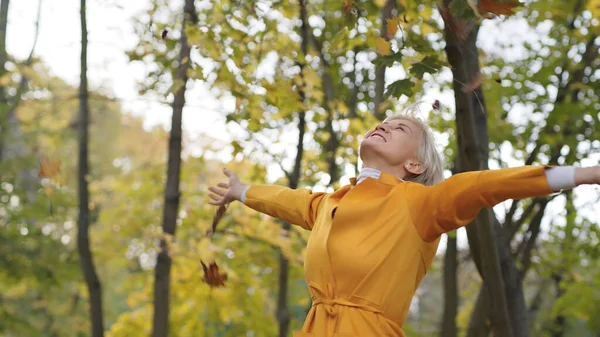 Glückliche Kaukasierin, die im Park gelbe Herbstblätter schleudert und sich herumdreht — Stockfoto