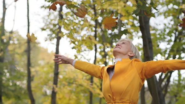 Glückliche Kaukasierin, die im Park gelbe Herbstblätter schleudert und sich herumdreht — Stockfoto