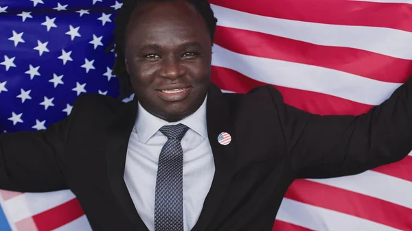 Portrait, young african american black man in formalwear with usa badge on the chest holding usa flag