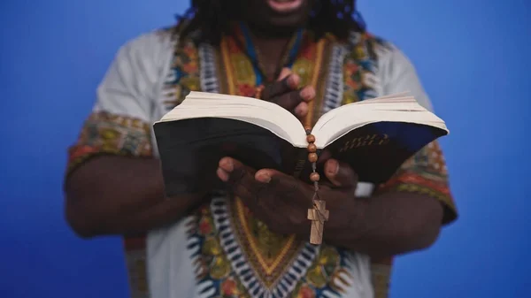 Hombre negro africano irreconocible en traje tradicional con rosario leyendo la Santa Biblia — Foto de Stock