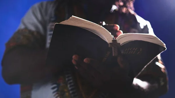 Неузнаваемый африканский черный мужчина в традиционной одежде с четками, читающими Библию — стоковое фото