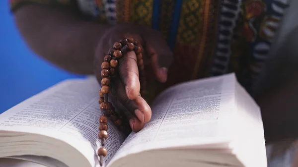 Unerkennbarer afrikanischer Schwarzer in traditioneller Kleidung mit Rosenkranz beim Lesen der Heiligen Bibel — Stockfoto