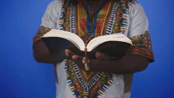 Hombre negro africano irreconocible en traje tradicional con rosario leyendo la Santa Biblia —  Fotos de Stock