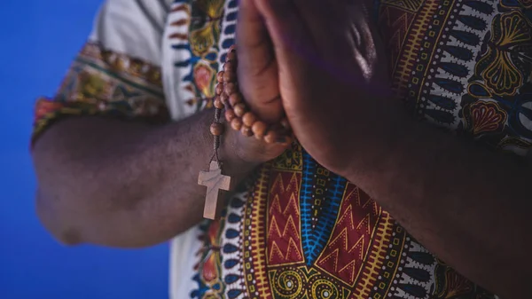 Unrecognizable African black man in traditional dress with rosary praying with hands over his chests — Stock Photo, Image