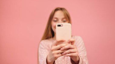 Beyaz bir kadın akıllı telefon kullanıyor ve fotoğraf çekiyor. Pembe arka planda izole edilmiş