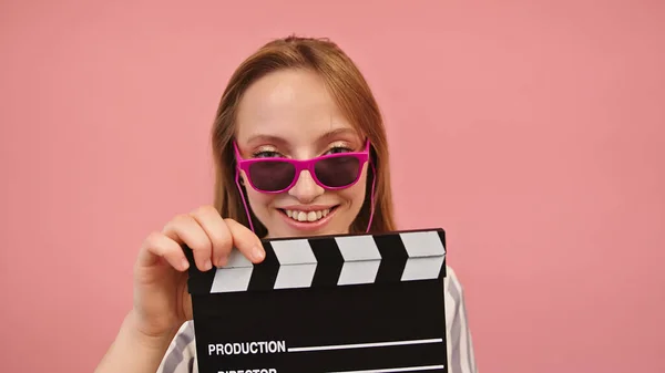 Mladá běloška s růžovými slunečními brýlemi a klasickým černým filmem clapperboard — Stock fotografie