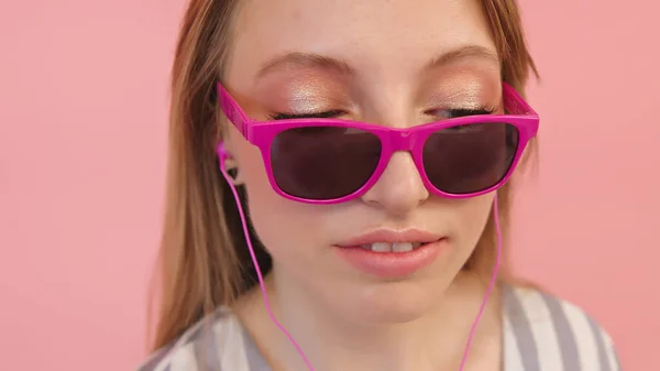 Mulher branca jovem com óculos de sol ouvindo a música usando fones de ouvido. Isolado em fundo rosa, close-up — Fotografia de Stock