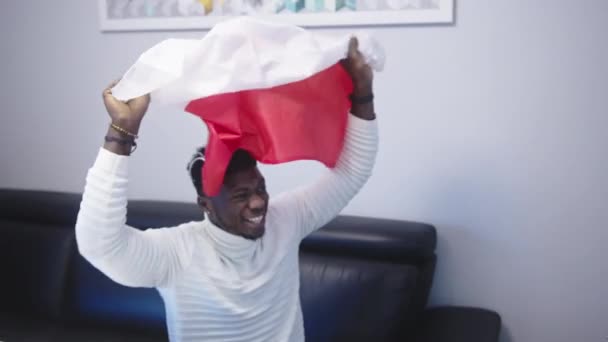 Young happy black man man with polish flag watching footbal game on tv — Stock Video