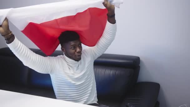 Jovem homem negro feliz com bandeira polonesa assistindo jogo de futebol na tv — Vídeo de Stock