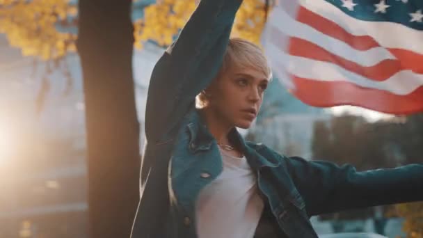 Mujer rubia joven con bandera de EE.UU. en el parque. Concepto de elecciones presidenciales justas — Vídeos de Stock