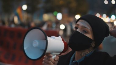 Covid-19 tecrit önlemlerine karşı gösteriler. Yüz maskeli genç bir kadın hoparlöre bağırıyor.