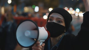  Yüzünde tıbbi maske olan genç, kısa saçlı kadın sokak protestolarında hoparlörlere slogan at. 