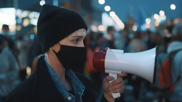 Joven mujer de pelo corto con máscara médica en la cara gritar consignas a altavoz en la protesta callejera — Foto de Stock