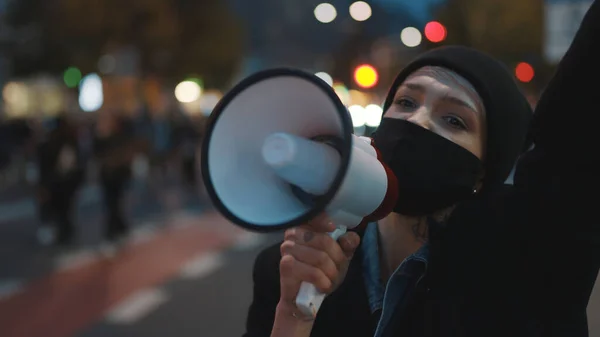 Νεαρή γυναίκα με μάσκα προσώπου φωνάζοντας συνθήματα σε μεγάφωνο σε διαδήλωση στο δρόμο — Φωτογραφία Αρχείου