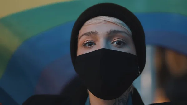 Retrato de mujer joven con máscara facial y bandera de arco iris. Concepto de aceptación de la orientación sexual, protesta durante el brote de coronavirus — Foto de Stock