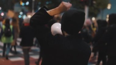 Covid-19 tecrit önlemlerine karşı gösteriler. Kalabalıktaki genç kadın hoparlöre atlayıp bağırıyor.