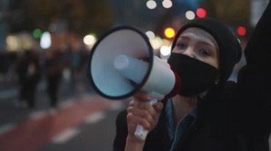 Covid-19 tecrit önlemlerine karşı gösteriler. Yüz maskeli genç bir kadın hoparlöre bağırıyor.