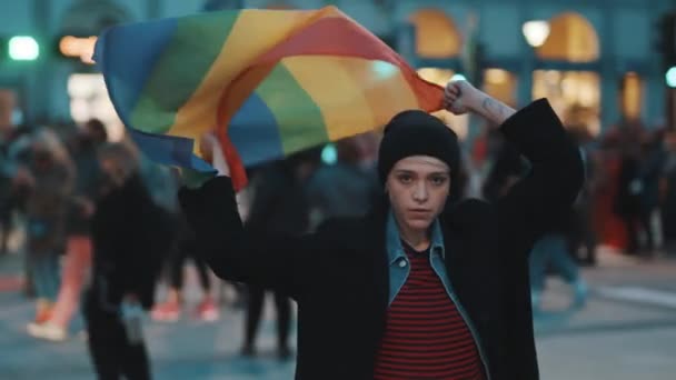 Молодая женщина на протесте размахивает радужным флагом гордости. Демонстрации во время вспышки ковида-19 и требования равных прав — стоковое видео
