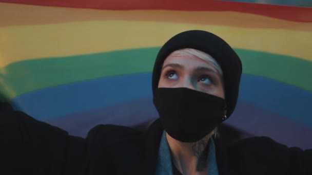 Egy fiatal nő arcmaszkkal és szivárvány zászlóval. A szexuális irányultság elfogadásának koncepciója, tiltakozás a koronavírus kitörése alatt — Stock videók