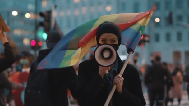 顔のマスクをした女性が虹の旗を持ちながらメガホンに向かって話す。判決に対する抗弁 — ストック動画