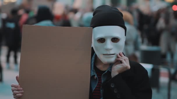 Νεαρή γυναίκα αφαιρεί θεατρική μάσκα κρατώντας μαύρο χαρτόνι μέσα στο πλήθος. Διαμαρτυρία κατά των διακρίσεων — Αρχείο Βίντεο