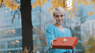 Beyaz, sarışın, kısa saçlı bir kadın hediye paketi ve kurdele veriyor. En iyi doğum günü hediyesi