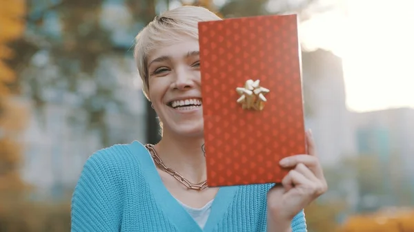 Mujer joven con enorme sonrisa sosteniendo regalo al aire libre — Foto de Stock