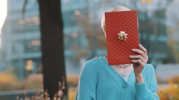 Jonge vrouw onthullen haar gezicht achter de geschenkdoos in het park — Stockvideo