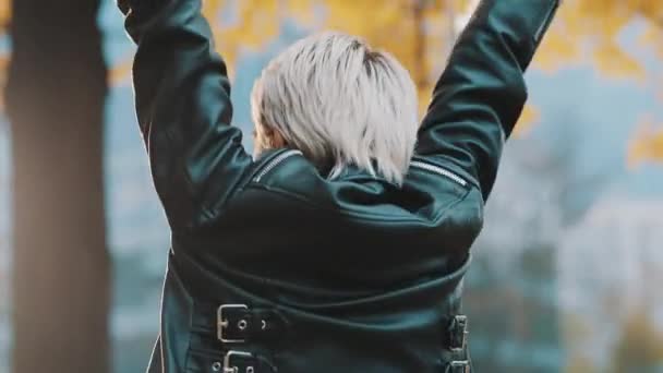 Jovem mulher caucasiana feliz em jaqueta de couro pulando e girando no parque no dia de outono — Vídeo de Stock