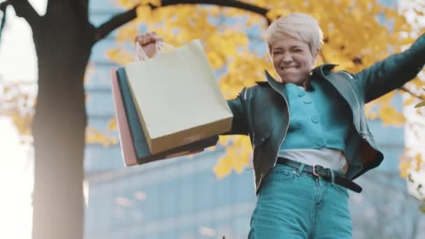 Happy young woman with shopping bags jumping and spinning in front of shoping mall — Stock Video