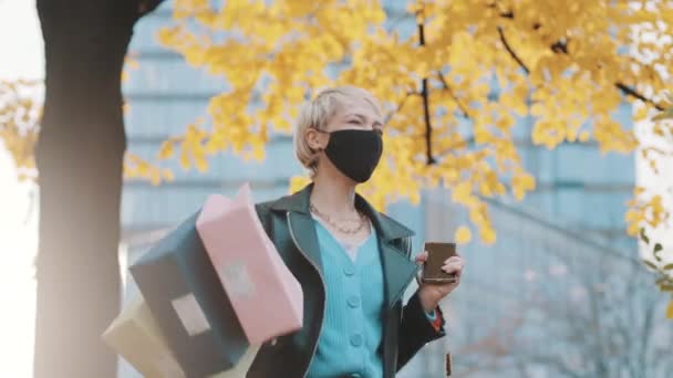 Excited young woman with face mask jumping with shopping bags in front of the shopping mall — Stock Video