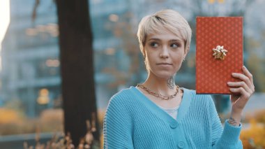 Şaşırmış yüz ifadesine sahip genç bir kadın dışarıda hediyesini tutuyor.