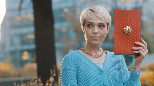 Jonge vrouw met verrast gezicht expressie houden geschenk buiten — Stockfoto