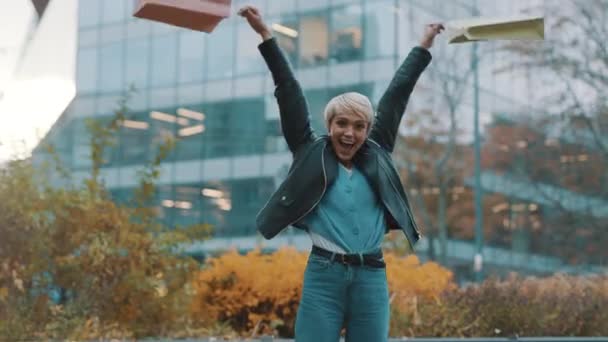 Fröhliche junge Frau mit Einkaufstüten lacht aufgeregt vor dem Einkaufszentrum — Stockvideo