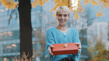 Beyaz, sarışın, kısa saçlı bir kadın hediye paketi ve kurdele veriyor. En iyi doğum günü hediyesi