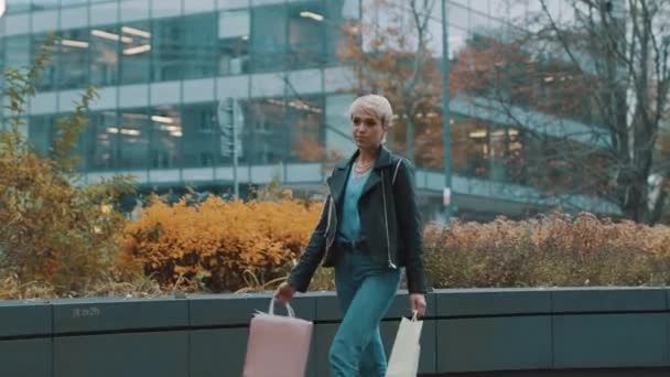 Glad ung kvinna promenader i casual kläder med shoppingväskor och leende — Stockvideo