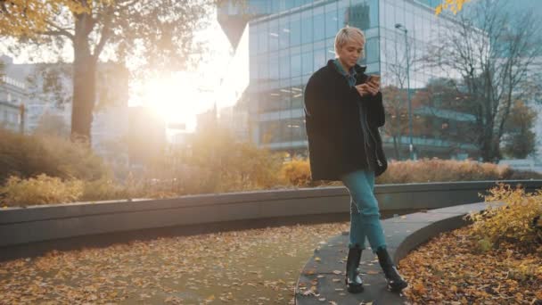 가을에 시청 건물 앞에서 도시 공원에서 전화를 사용하고 있는 젊은 코카서스 여성 — 비디오