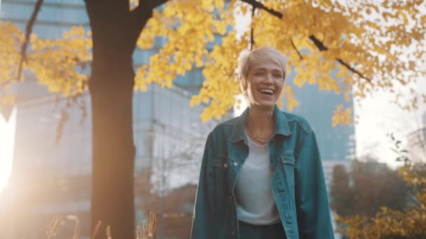 Gelukkig jong blond vrouw in denim jasje lachen hard onder de boom met herfst bladeren — Stockvideo