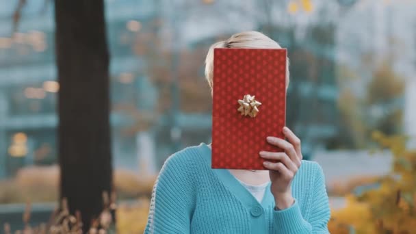 Young woman revealing her satisfied face behind the gift box in the park — Stock Video