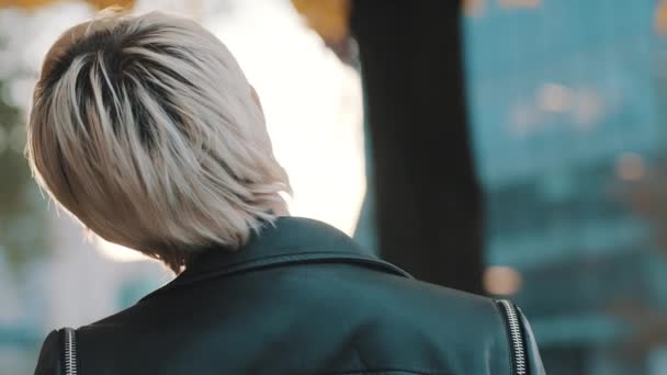 Vacker kort hår blond kvinna i läder jacka och solglasögon vänder huvudet mot kameran — Stockvideo