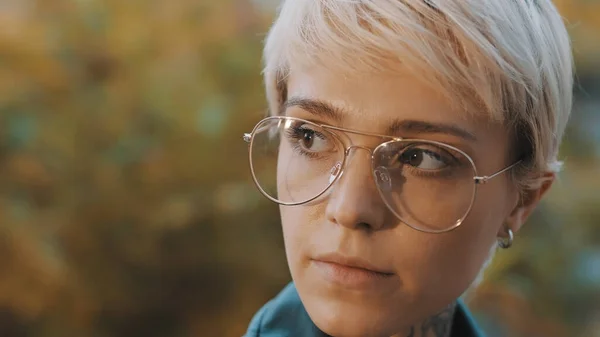 Portret van een jonge blanke blonde vrouw met kort haar en een bril in het park — Stockfoto